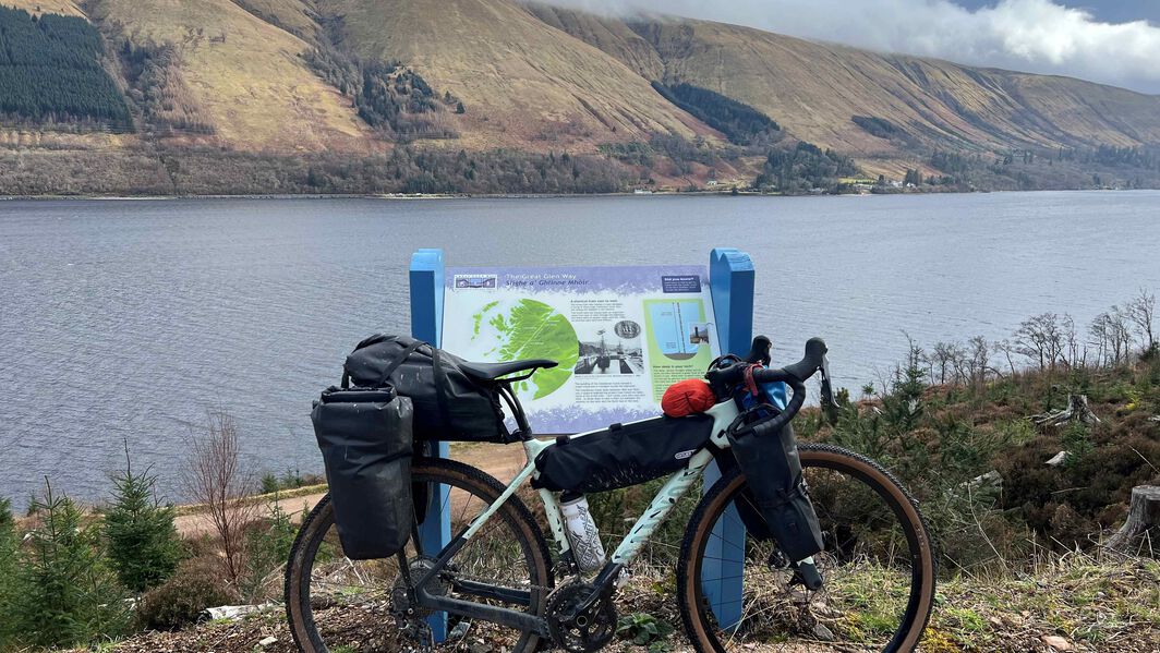 Fully loaded Canyon gravel bike parked by a lake with panniers and bikepacking gear, representing how to plan bikepacking routes and trips in the wild